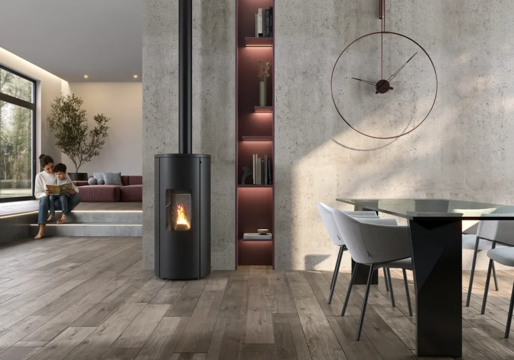 Rendering 3D di una stufa cilindrica AMG con scarico coassiale accesa in un soggiorno moderno accanto a un tavolo da pranzo.