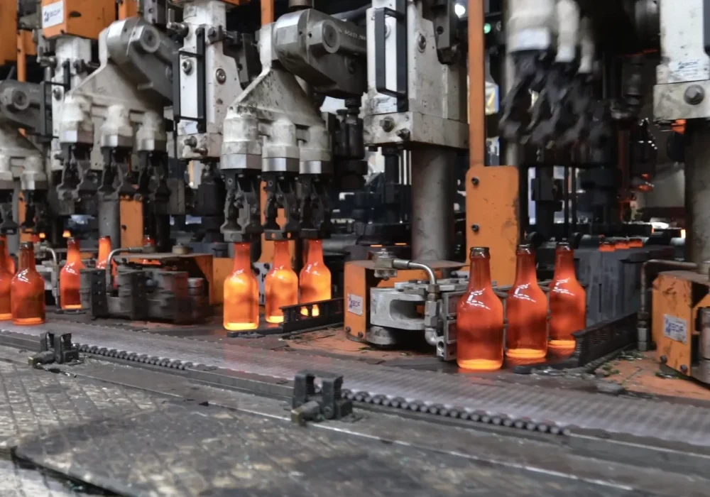 Macchinario BDF Industries in funzione mentre modella bottiglie di vetro cavo ancora incandescenti sulla linea di produzione